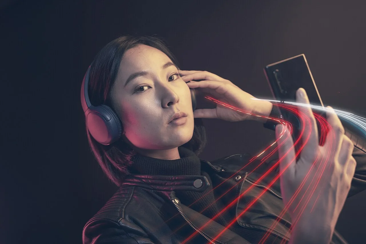 A woman wearing over-ear headphones uses a smartphone while listening to music.