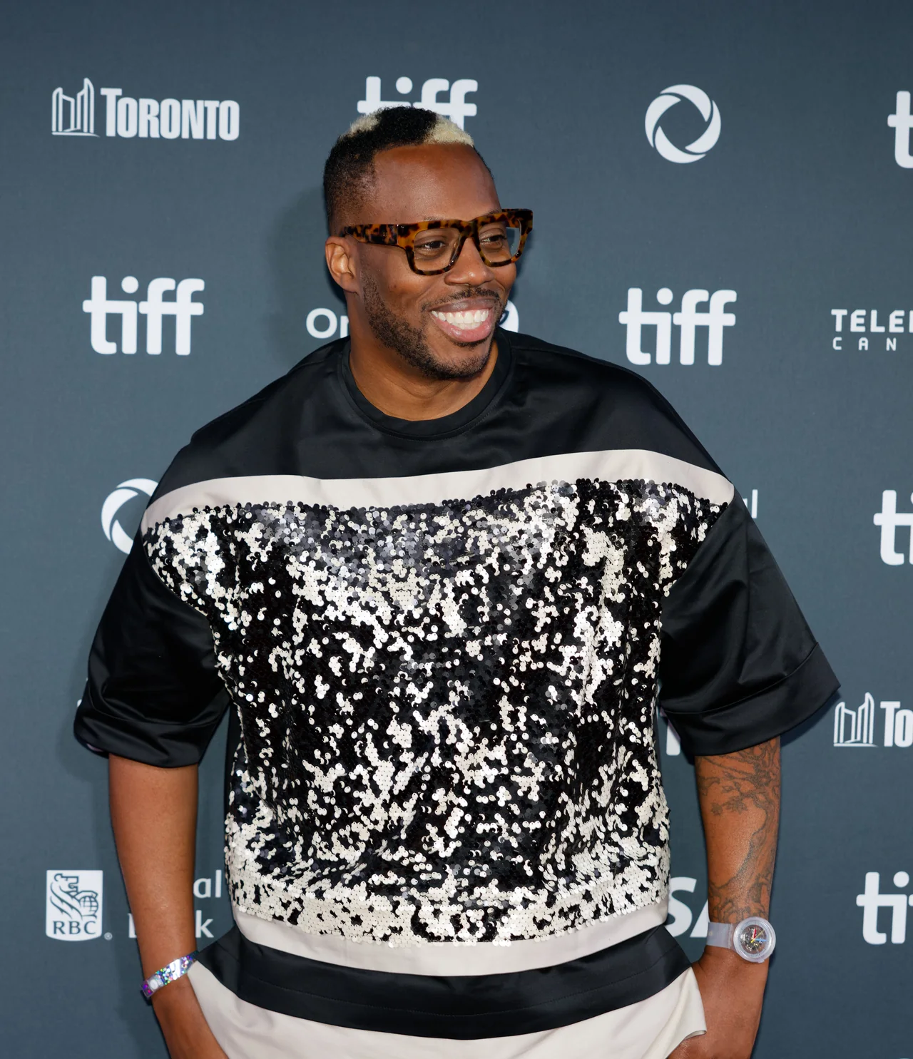 Kardinal Offishall smiles in glasses at the Toronto International Film Festival in front of a TIFF backdrop.
