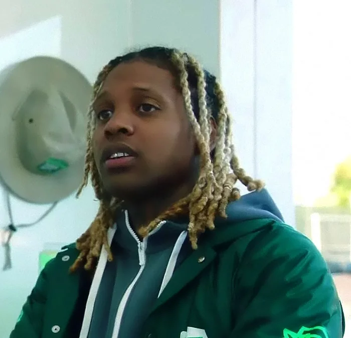 Lil Durk in a 2020 video still, wearing a green jacket and blond dreadlocks.