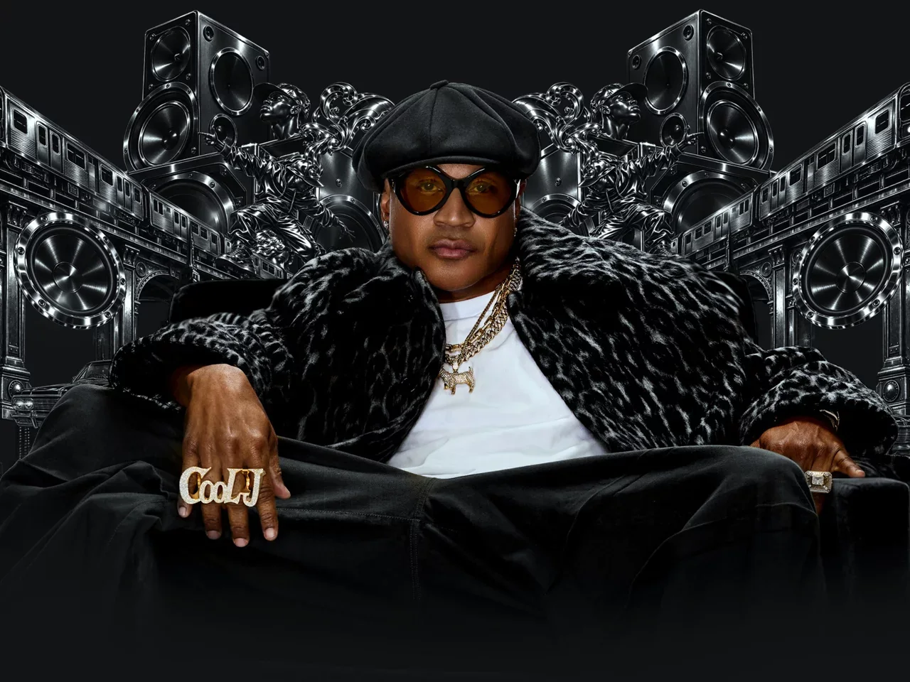 LL COOL J sits in dark glasses and a black jacket before a wall of speakers.