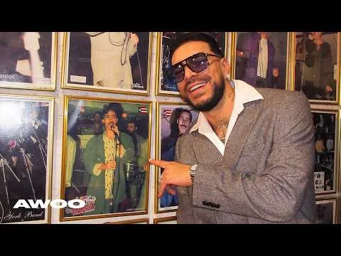 Ryan Castro points toward framed salsa photographs in the official “Lluvia (AWOO)” video cover.