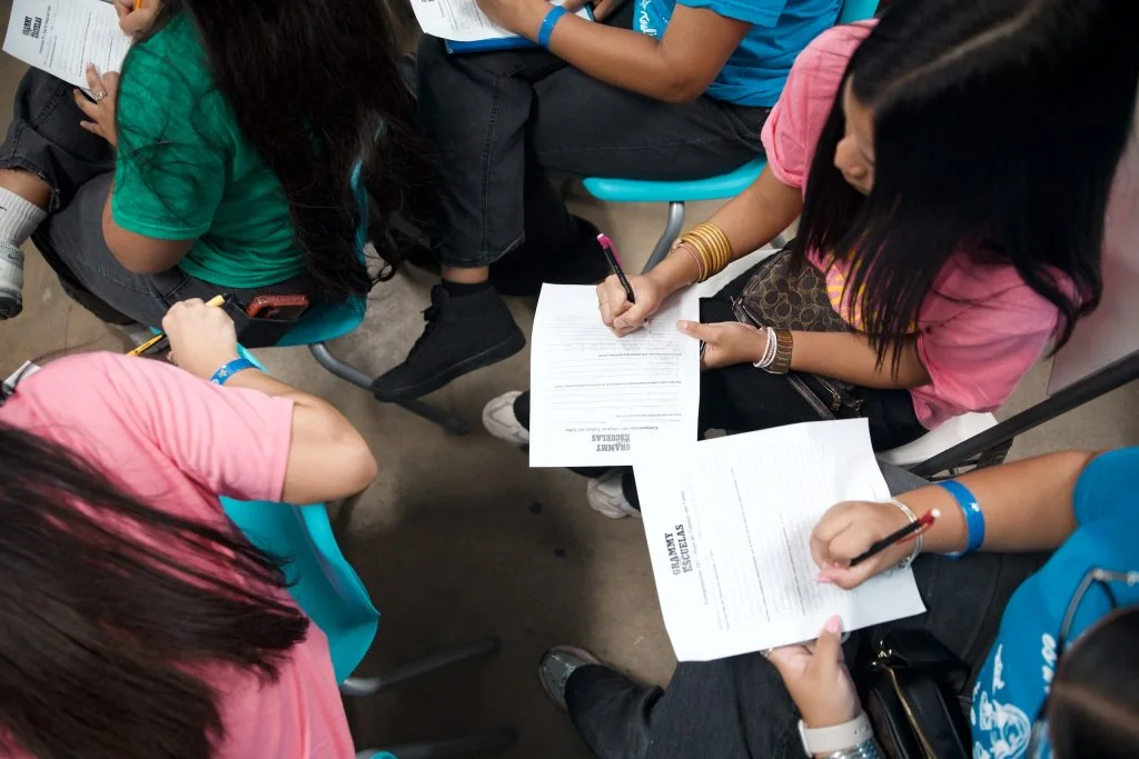 Students sit in a circle and write on workshop worksheets.