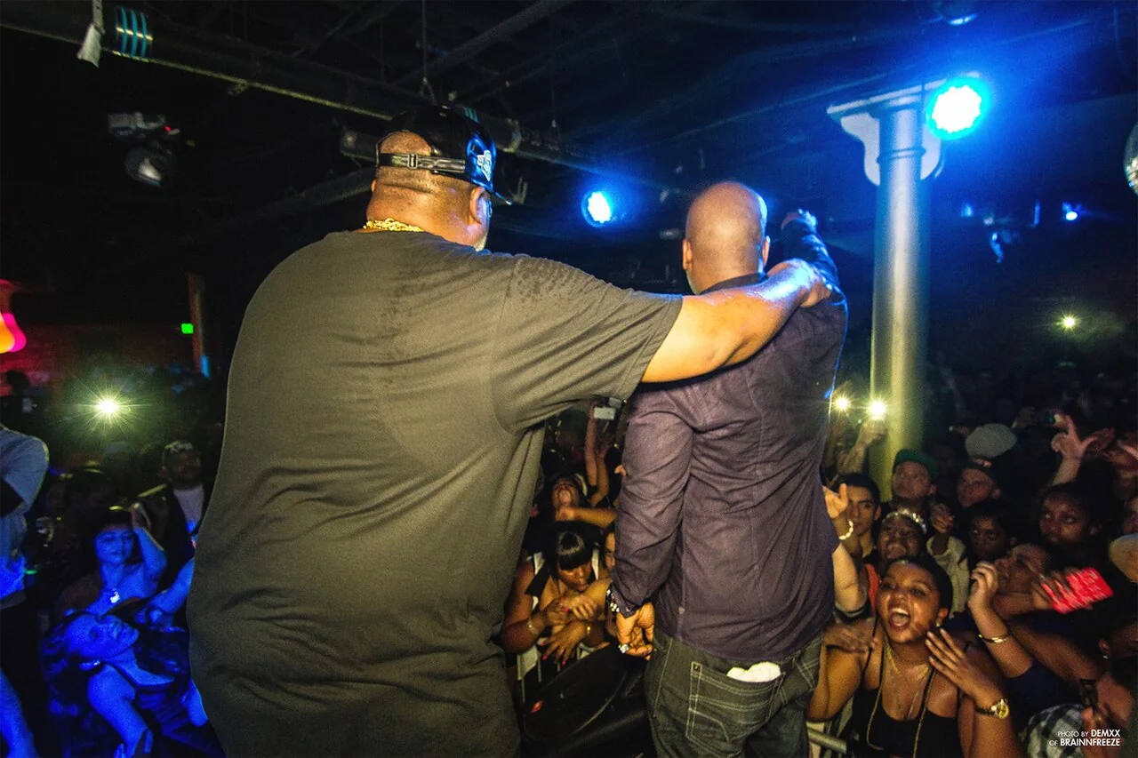 E-40 and Too $hort perform together in San Diego in January 2013, photographed from behind onstage.