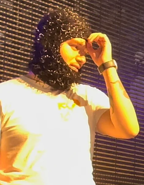 Yeat performs in a white shirt and dark knitted hat, holding a hand to his sunglasses.